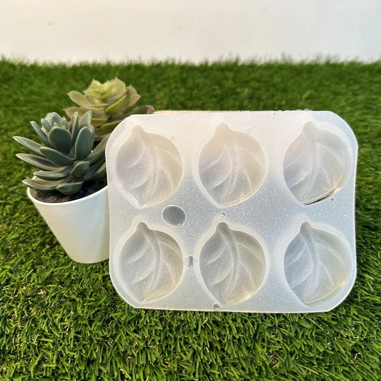 A silicone ice cube mold with six plant-shaped compartments, placed on green grass with a potted succulent plant nearby.