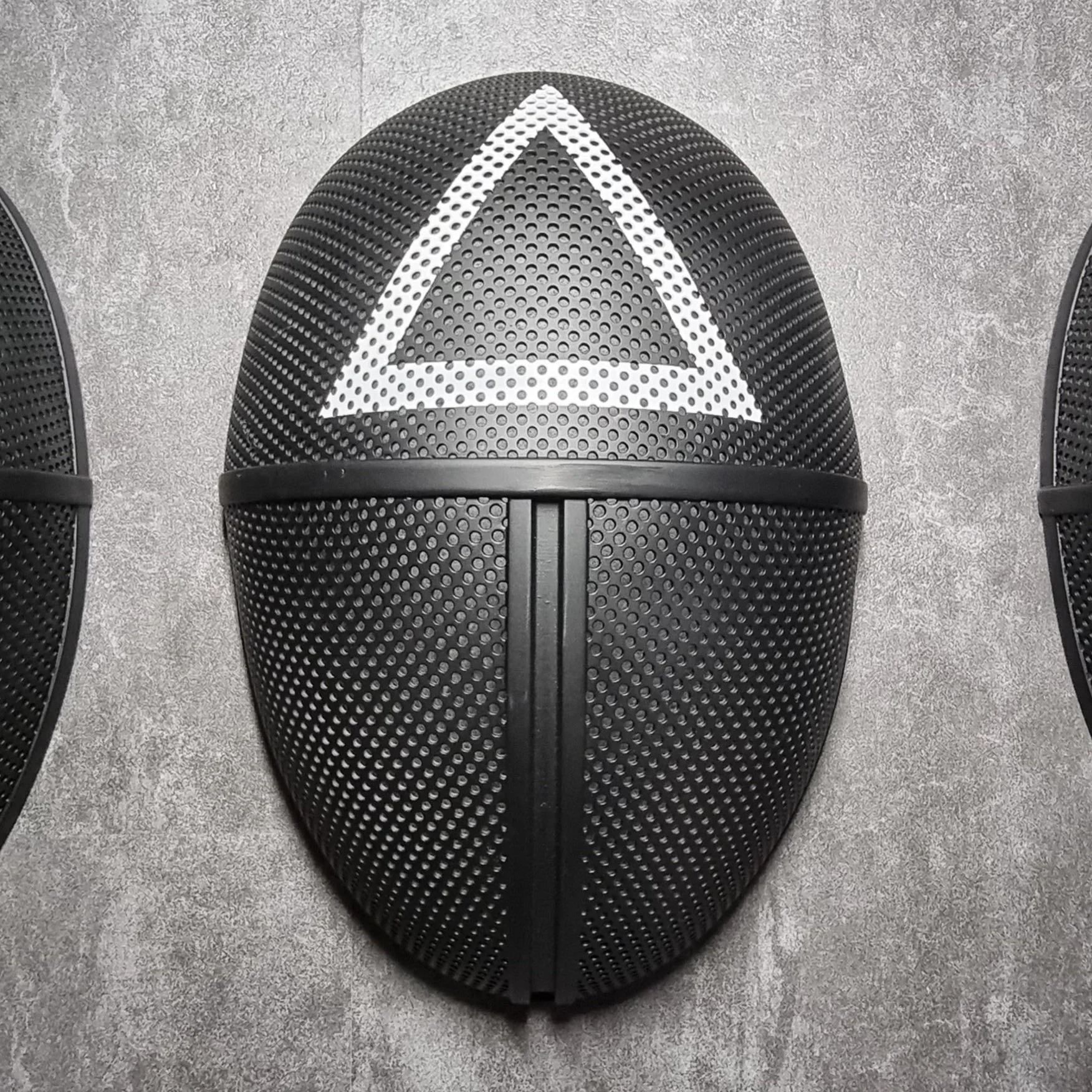 Black speaker with a white geometric triangle design on the top part, placed on a concrete surface.