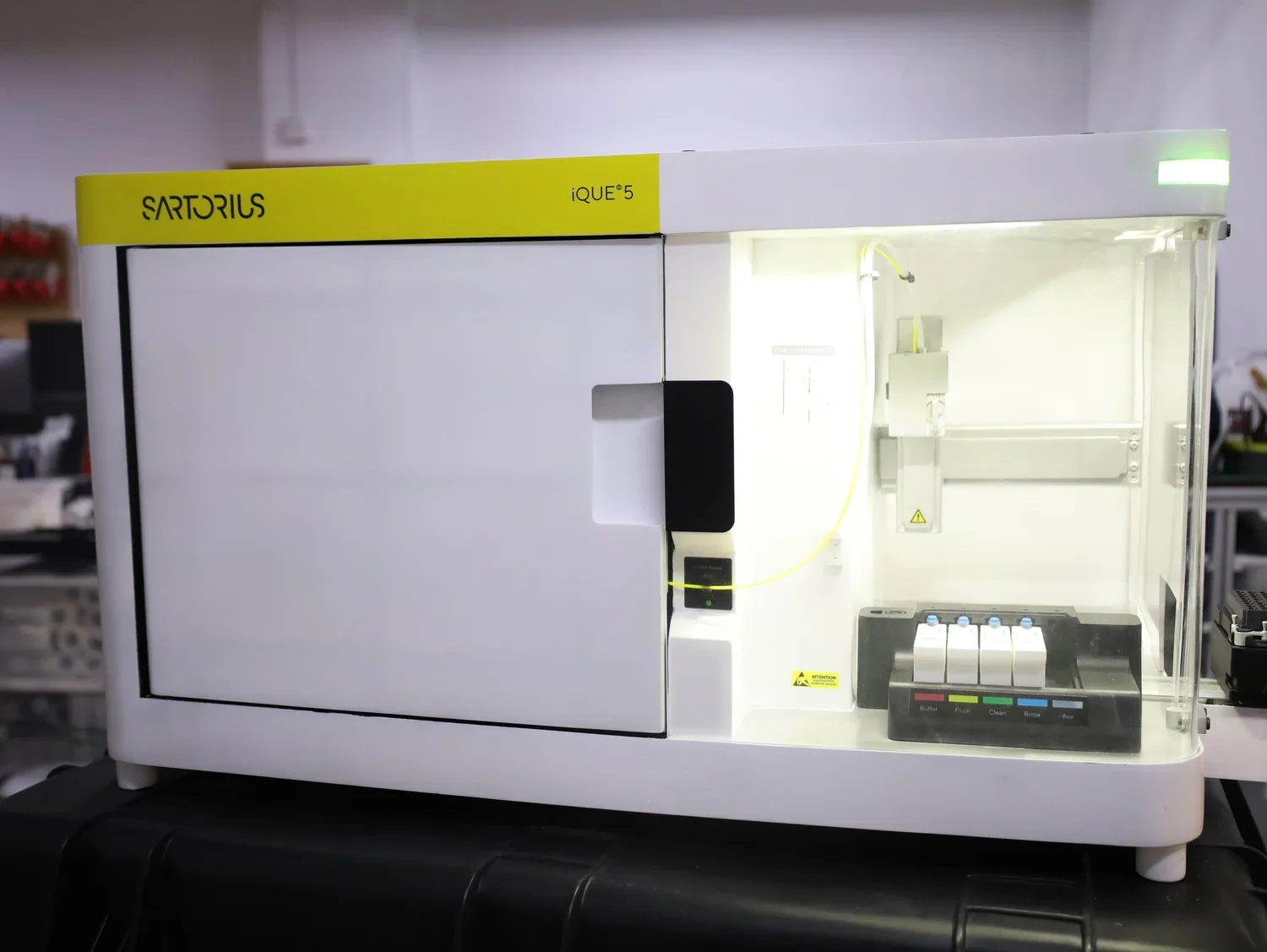 Laboratory instrument labeled 'Sartorius iQOE 5' with a white exterior, yellow and green accents, and a transparent front panel showing internal components and control buttons at the bottom.