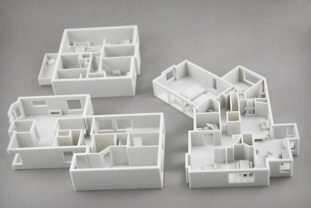 Three white architectural models of house layouts on a gray surface.