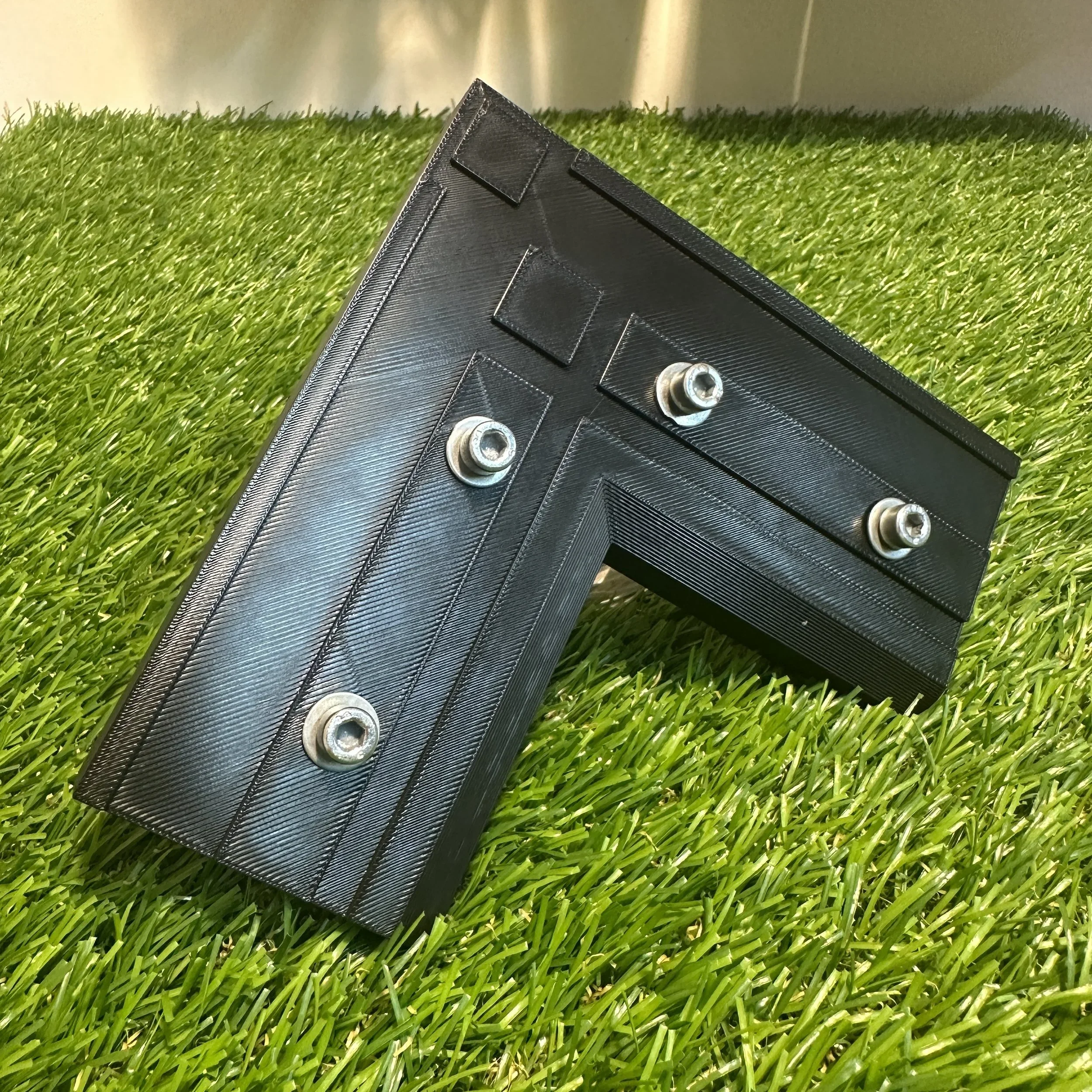 A black L-shaped electronic device with metal screws on a green grass surface.