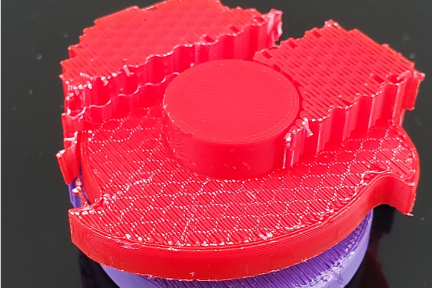 Close-up of a 3D-printed red object with circular and rectangular shapes on a dark background.