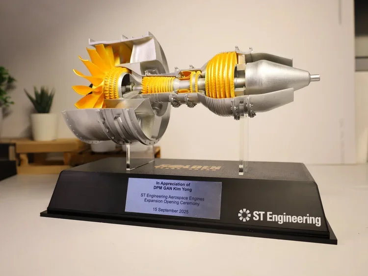 Model of a jet engine with yellow turbine blades and silver metallic casing on a black stand.
