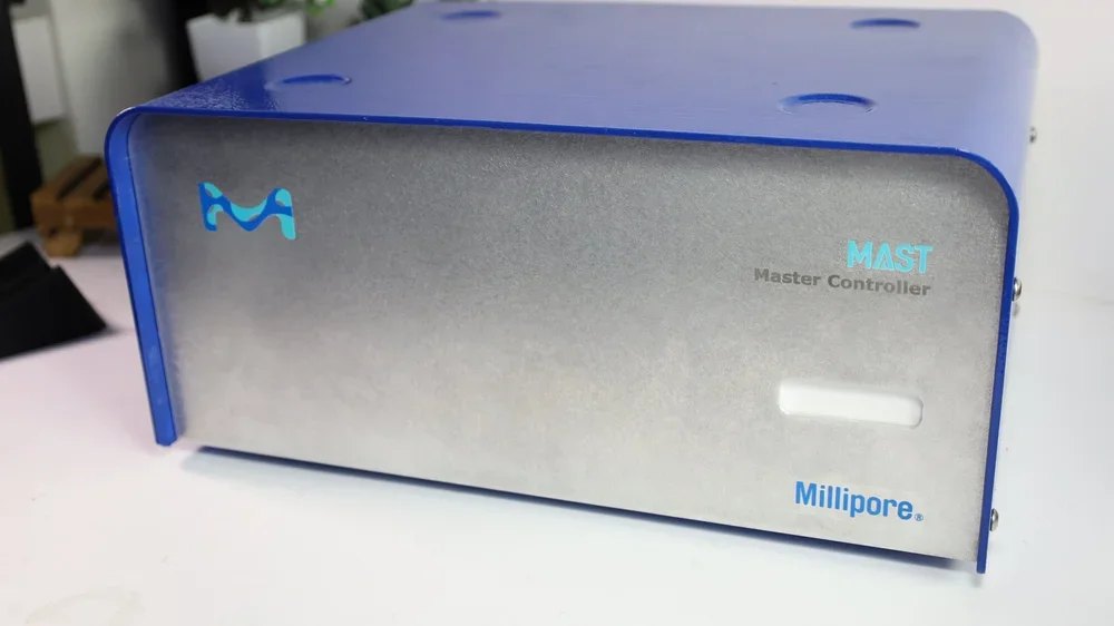 Millipore MAST Master Controller device, metallic front panel with blue side edges, placed on a white surface.