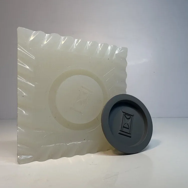 A piece of clear plastic packaging and a black and gray silicone mold with an hourglass symbol.