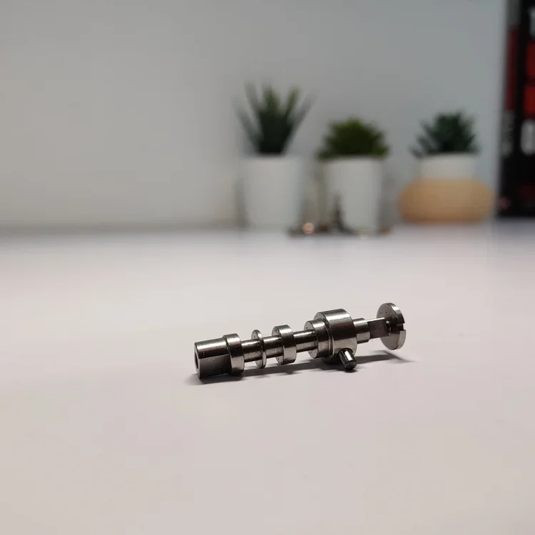 Metal component on a white surface with potted plants in the background.