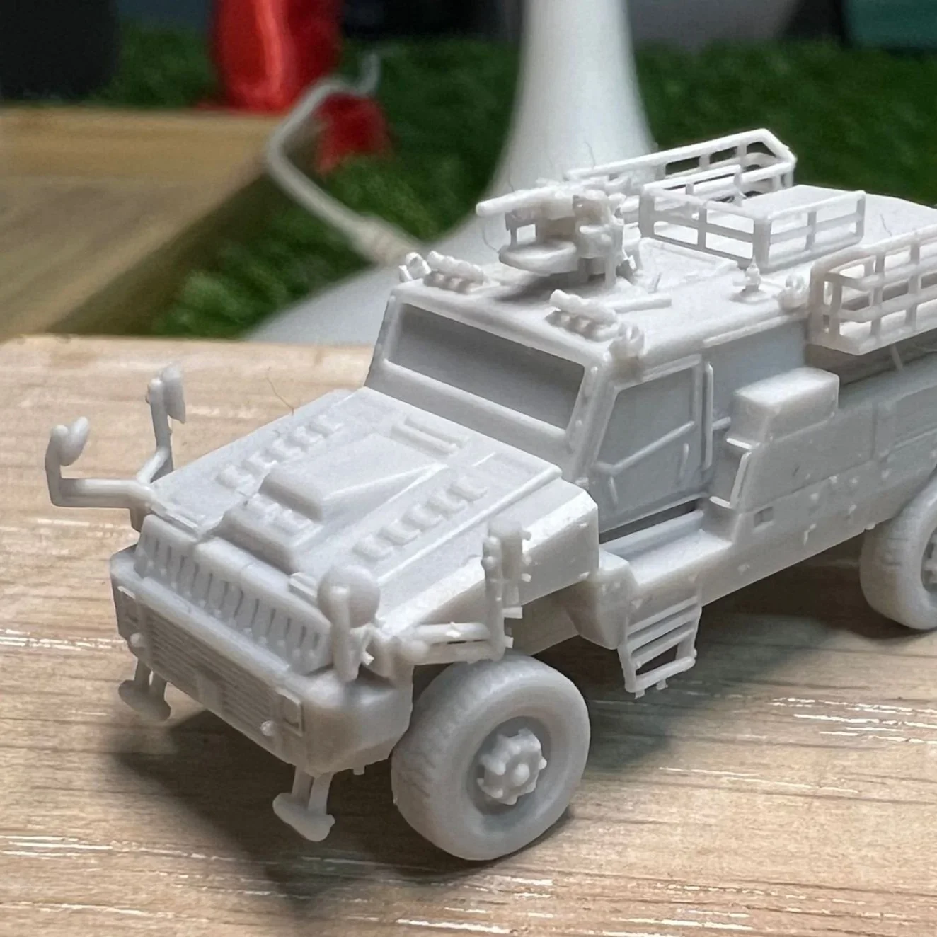 A small white model military truck with detailed features such as antennas, a ladder, and a roof rack, placed on a wooden surface.