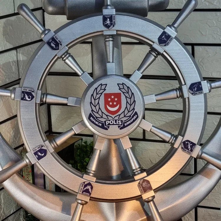 A ship's steering wheel with a police badge at the center, displaying the Singapore Police logo and the words "REPUBLIC POLIS SINGAPURA."