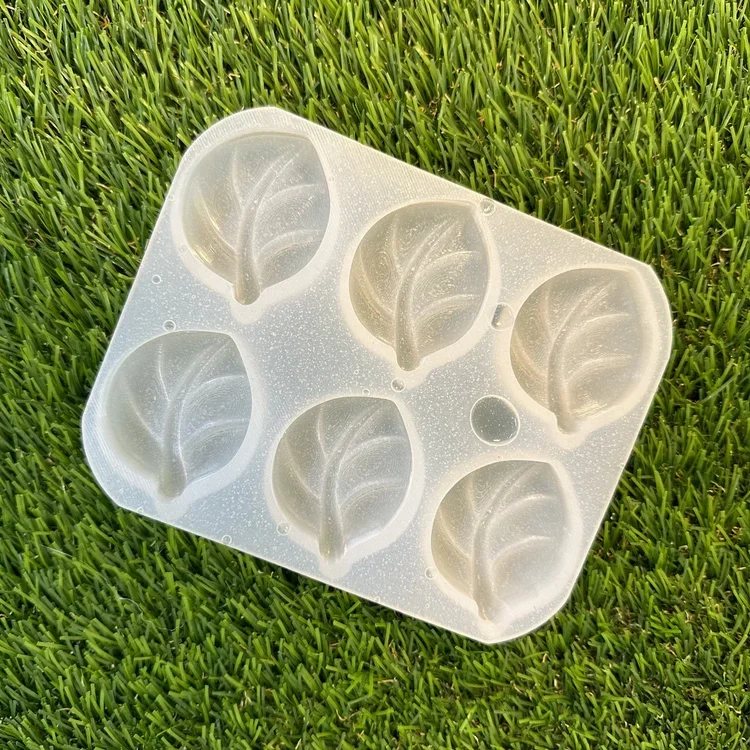 Silicone mold with six leaf-shaped cavities on a grassy surface.