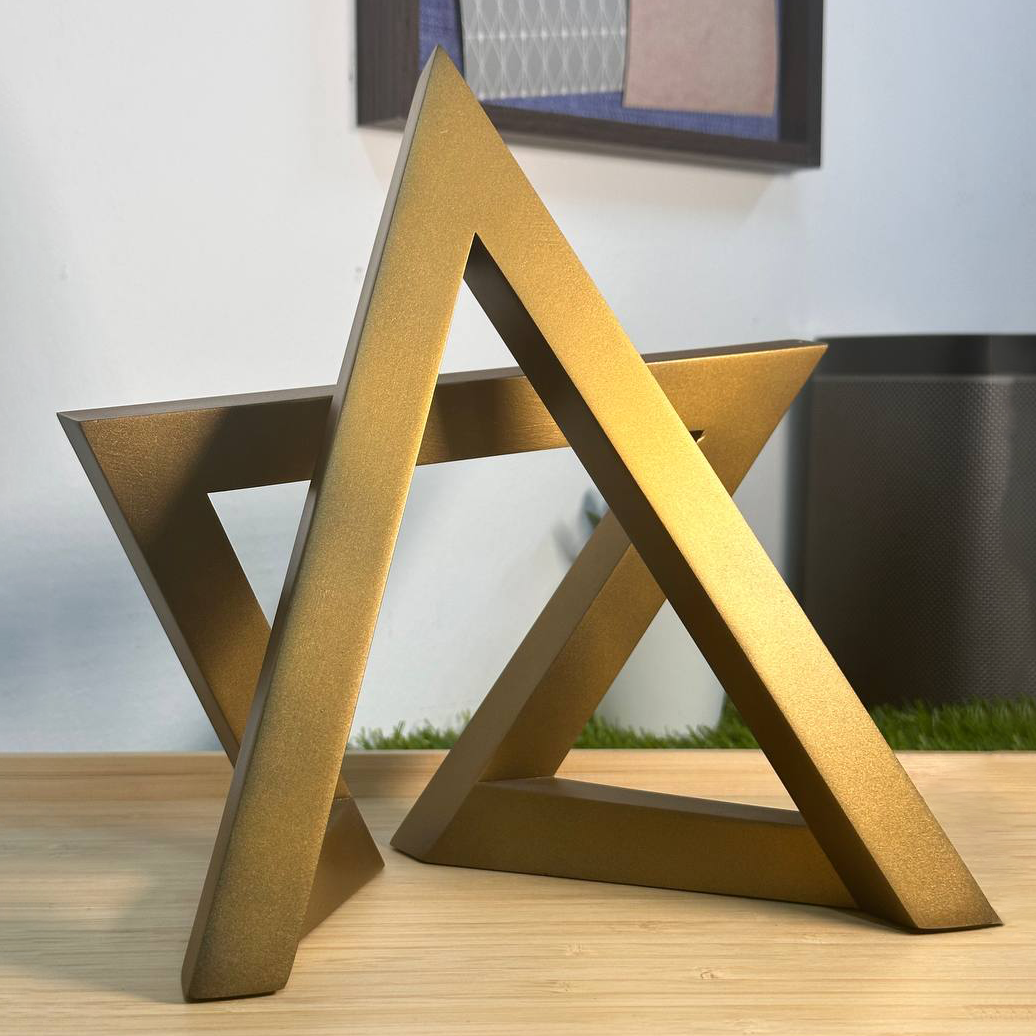 A gold, star-shaped trophy or sculpture placed on a wooden surface, with a framed picture and a black speaker or appliance in the background.