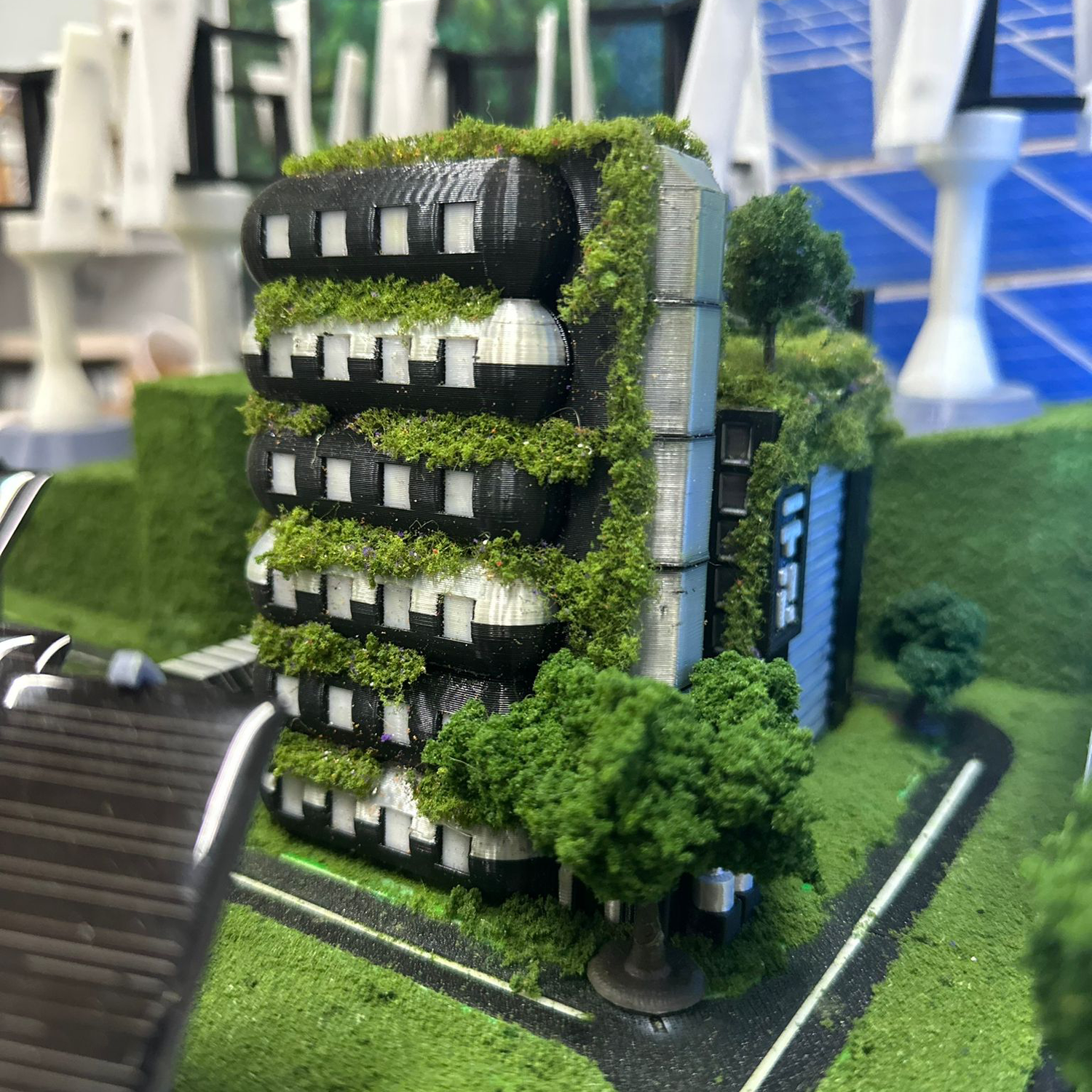 Miniature model of a modern office building covered with greenery, surrounded by miniature trees and a green landscape.
