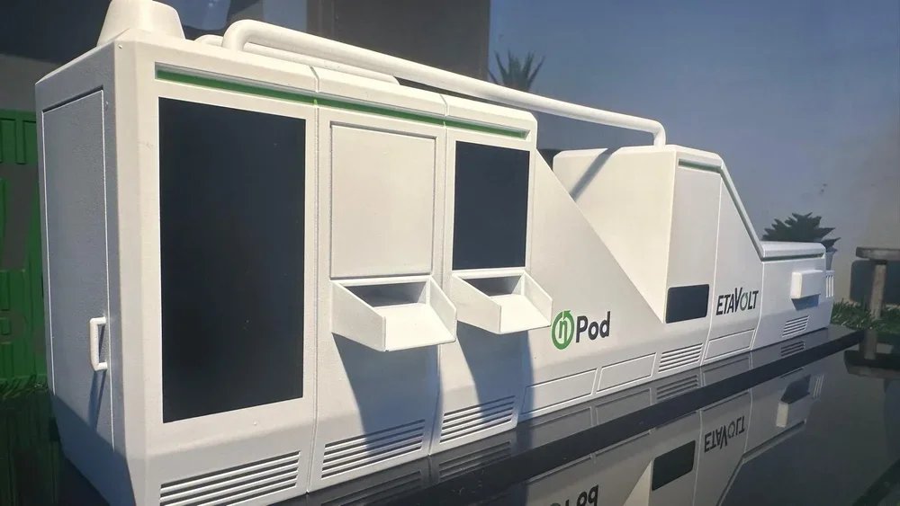 A futuristic-looking white electric vehicle charging station with multiple slots and display screens, labeled 'Pod' and 'ETAVOLT'.