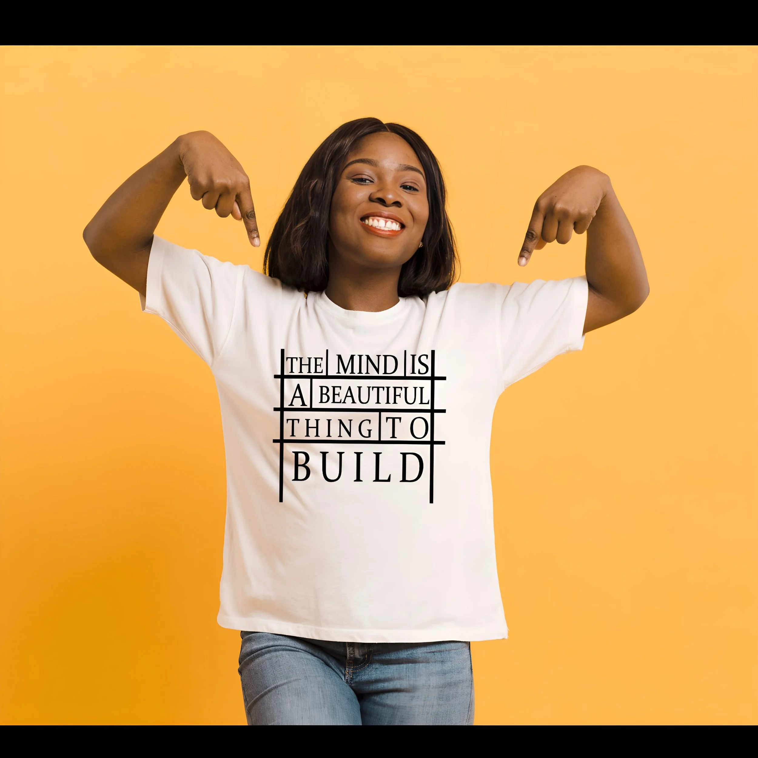 A woman smiling and pointing at her white t-shirt with the words "The mind is a beautiful thing to build" printed on it, standing against a yellow background.