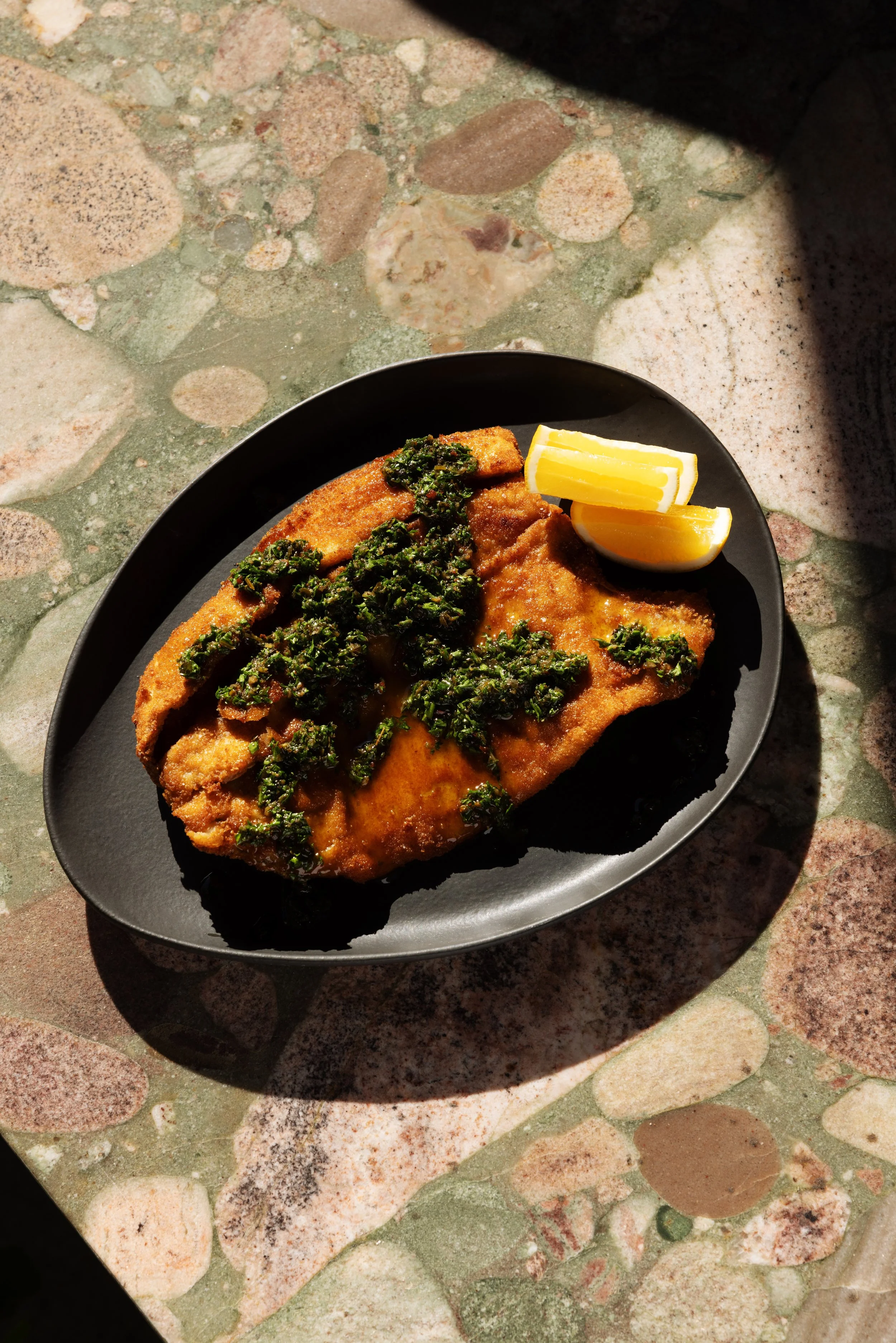 Fried Milanese fish filet food photography on black plate by Los Angeles food photographer Matt Francisco