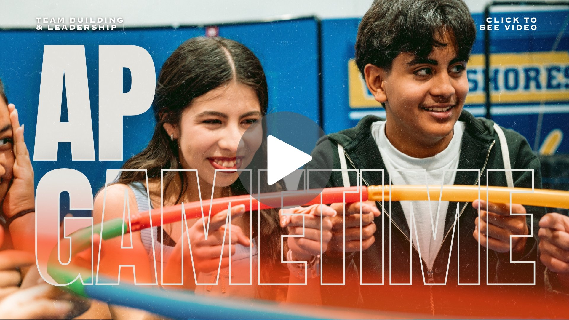 Group of teenagers holding colorful plastic hoops, smiling and having fun at an indoor team-building event with blue walls and motivational text in the background.