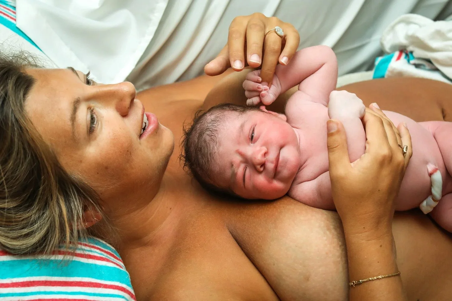 A woman holding a newborn baby during childbirth, lying in a hospital bed.