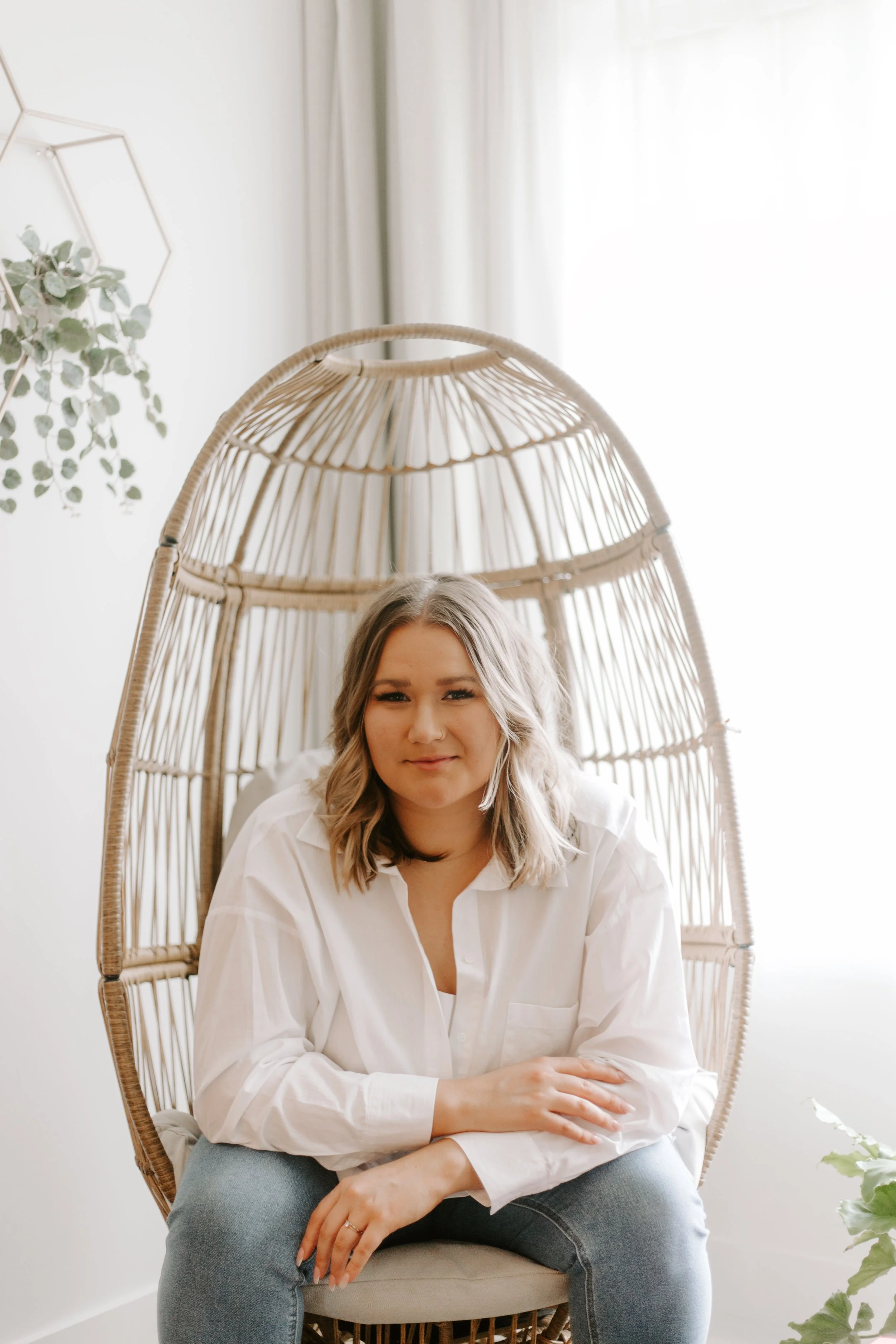 Smiling Tiia Alexandria sitting in wicker chair - light airy background