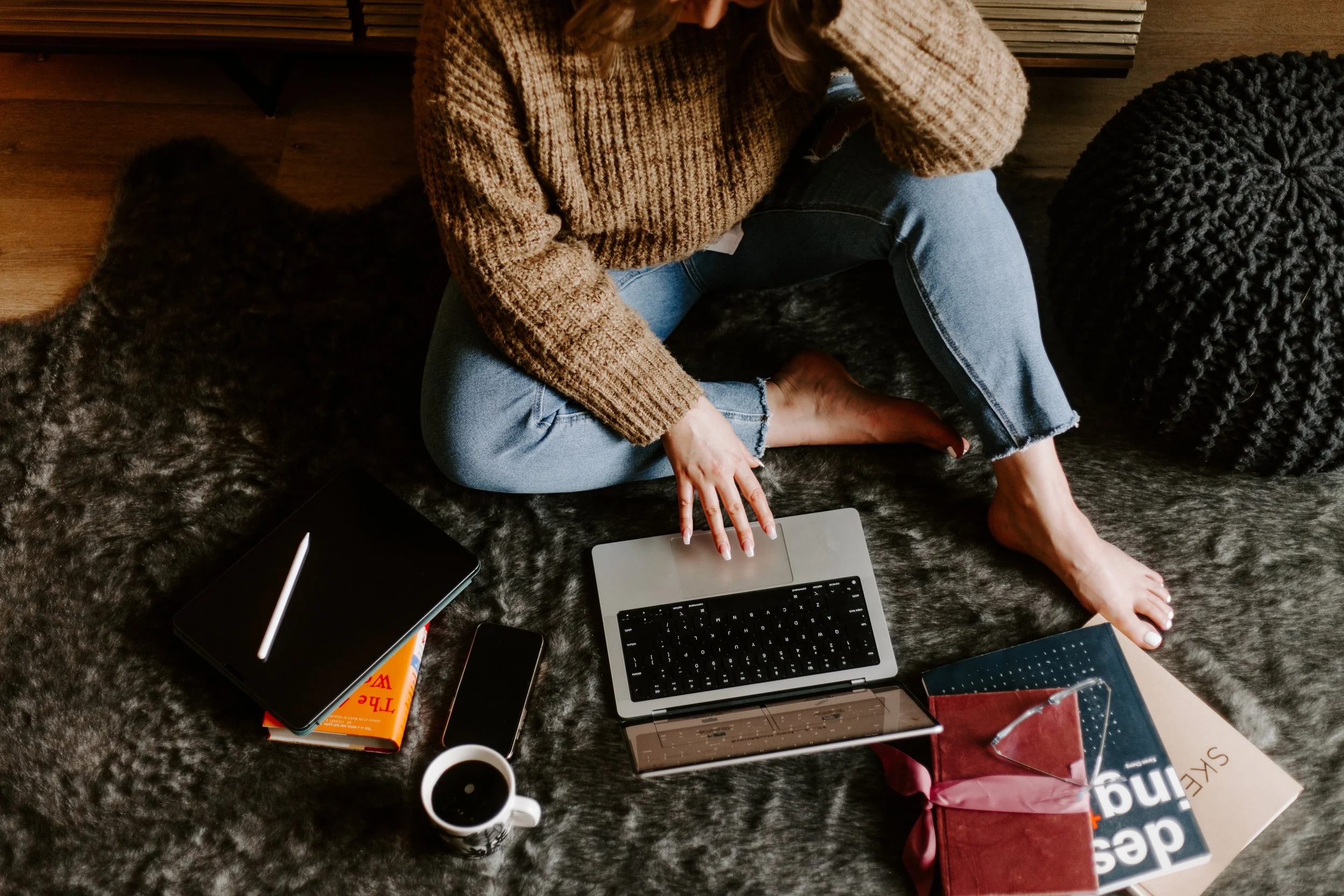 Overhead shot of woman working on laptop while sitting on floor surrounded by design books