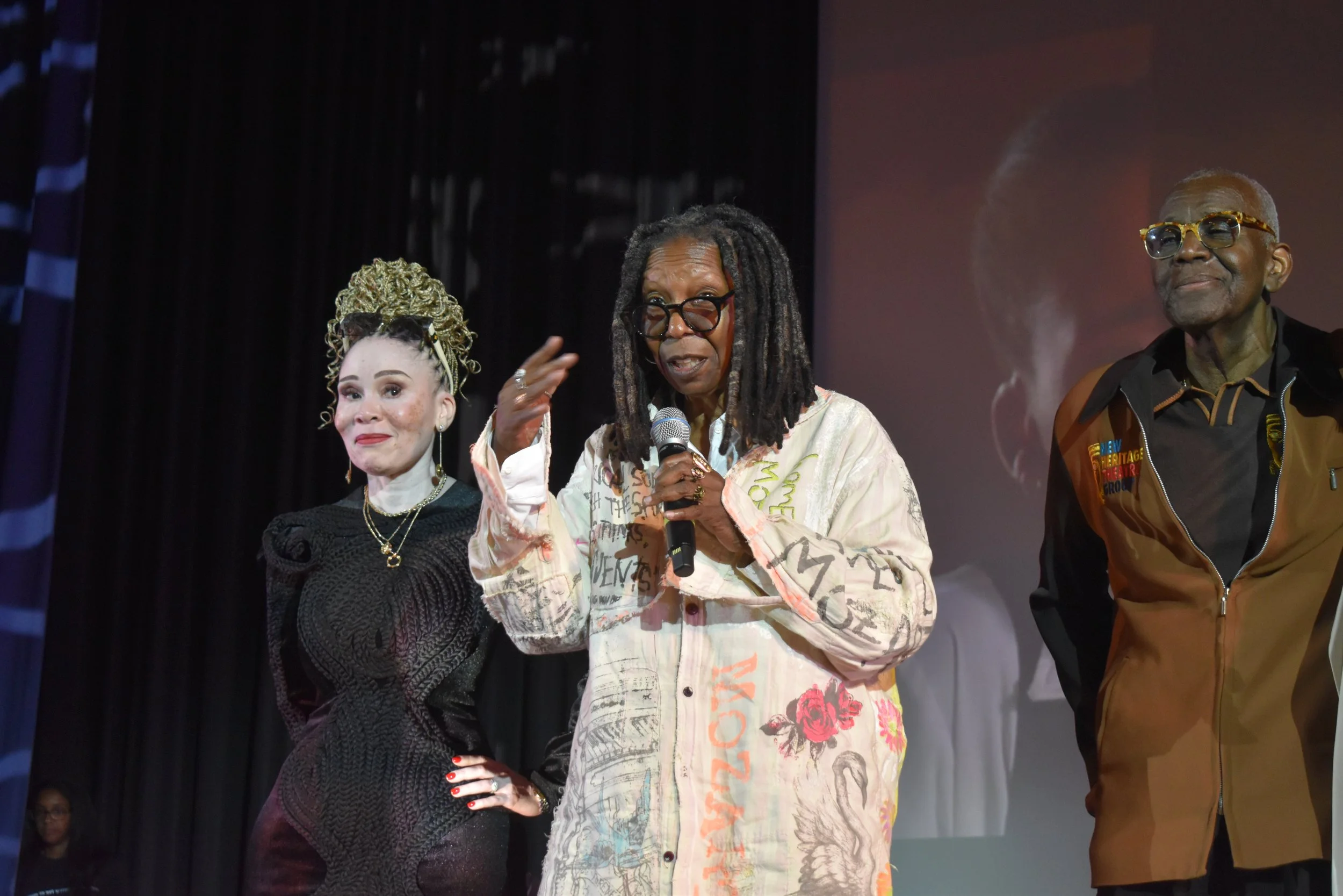 Whoopi Goldberg with Leleti Khumalo and Voza Rivers on the stage of the A. Philip Randolph High School