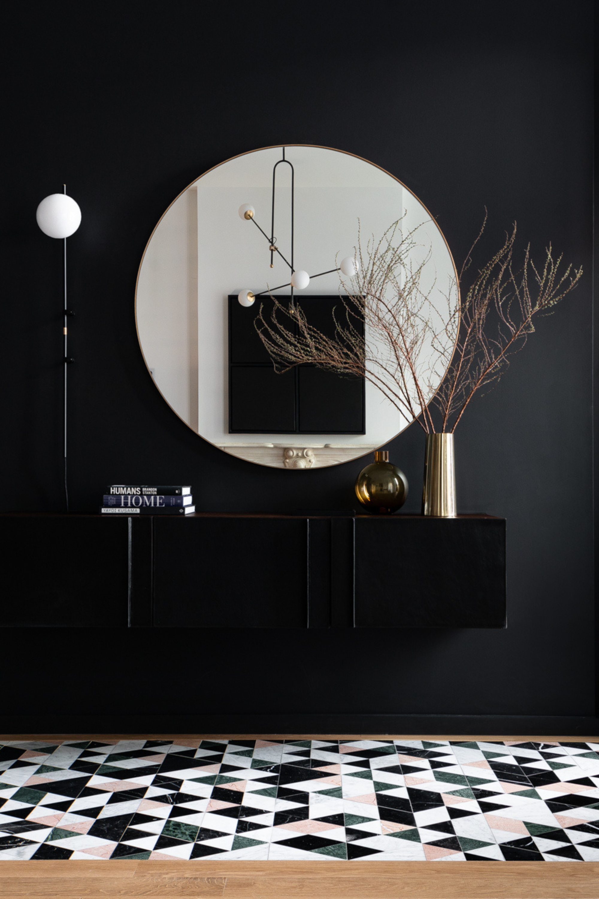 Entryway design by Elaine Santos Design with a black wall, large round mirror and wall light with a globe shade