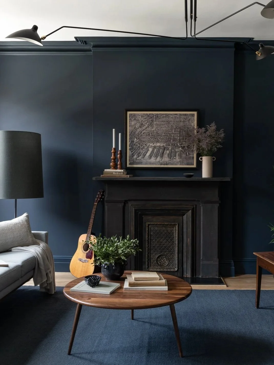 Livingroom painted in dark, moody blue with vintage fireplace, wood furniture, and modern lighting