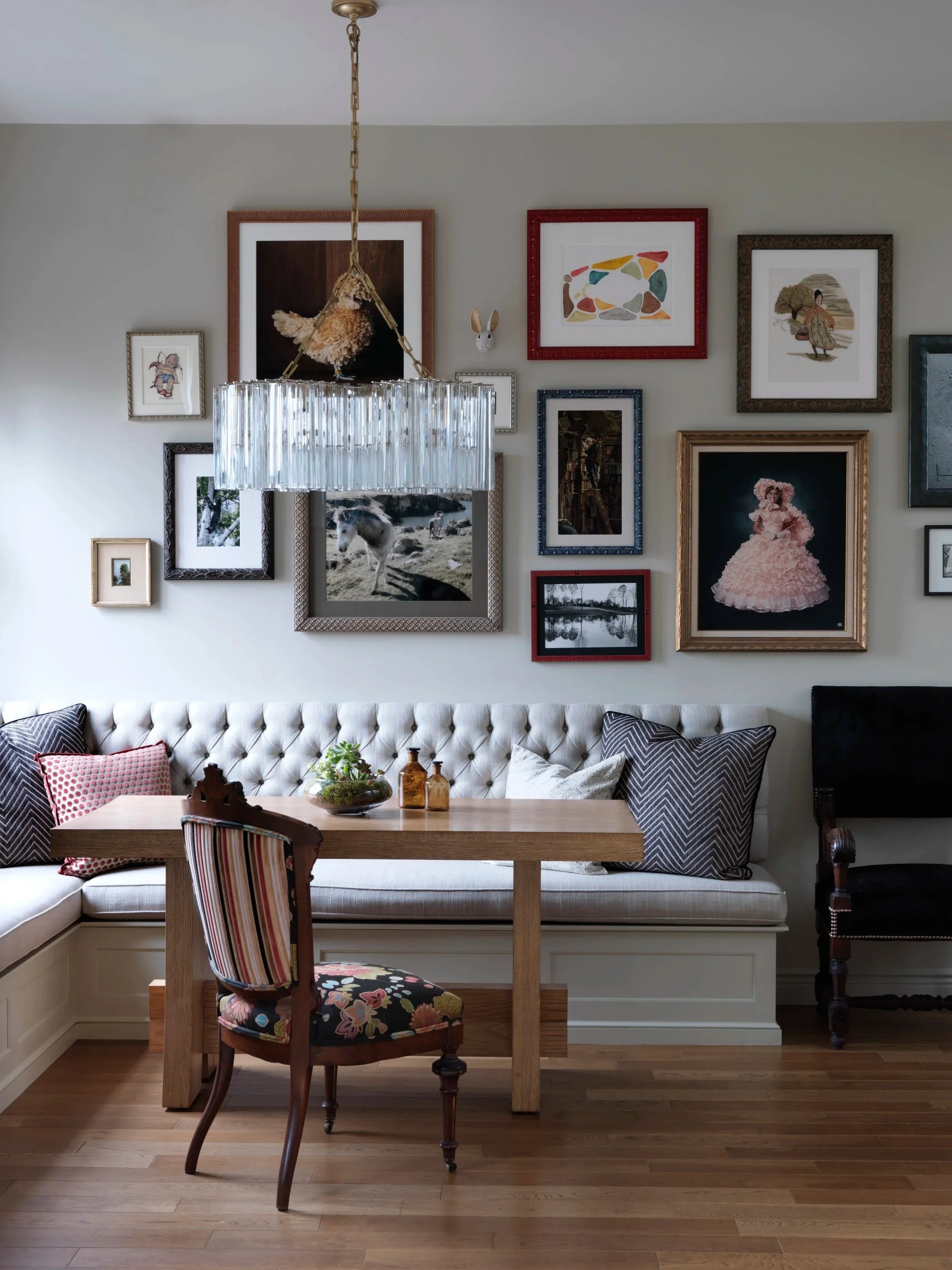 glass chandelier light hanging over wood table with upholstered bench seat and a gallery wall behind it