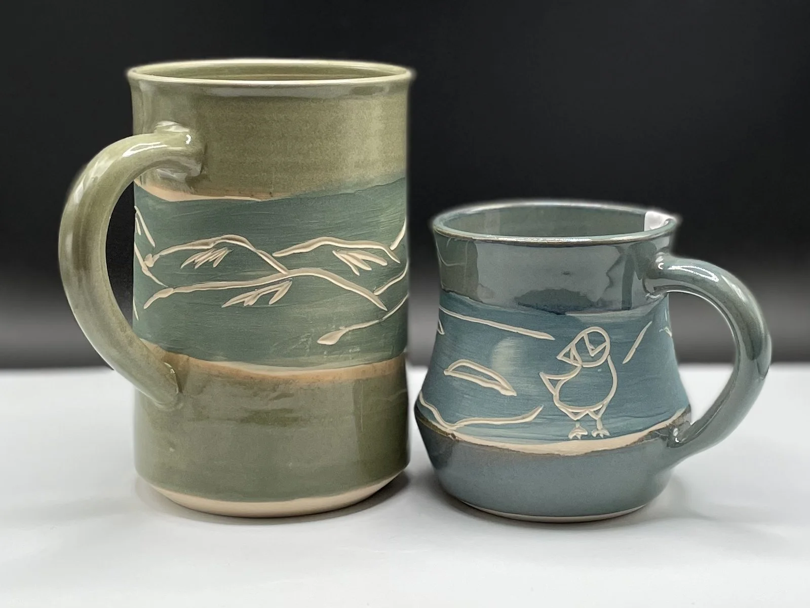 A ceramic cup with a textured, earthy glaze sit on a large, red rock outdoors with a blue sky in the background.