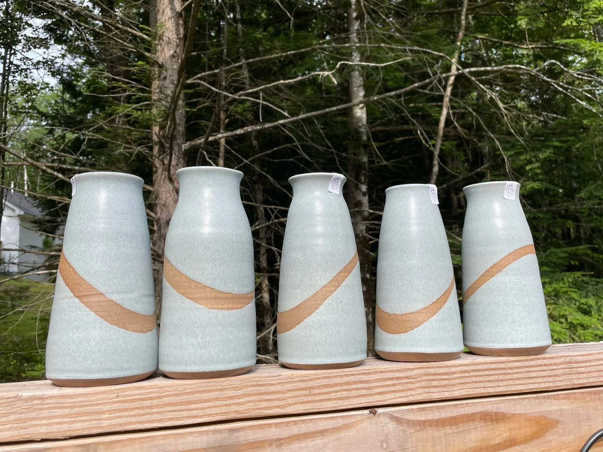Close-up of a ceramic mug with a wooden handle that is stamped with the text 'MOAB 09-05-21,' outdoors with a blurred background of trees and sky.
