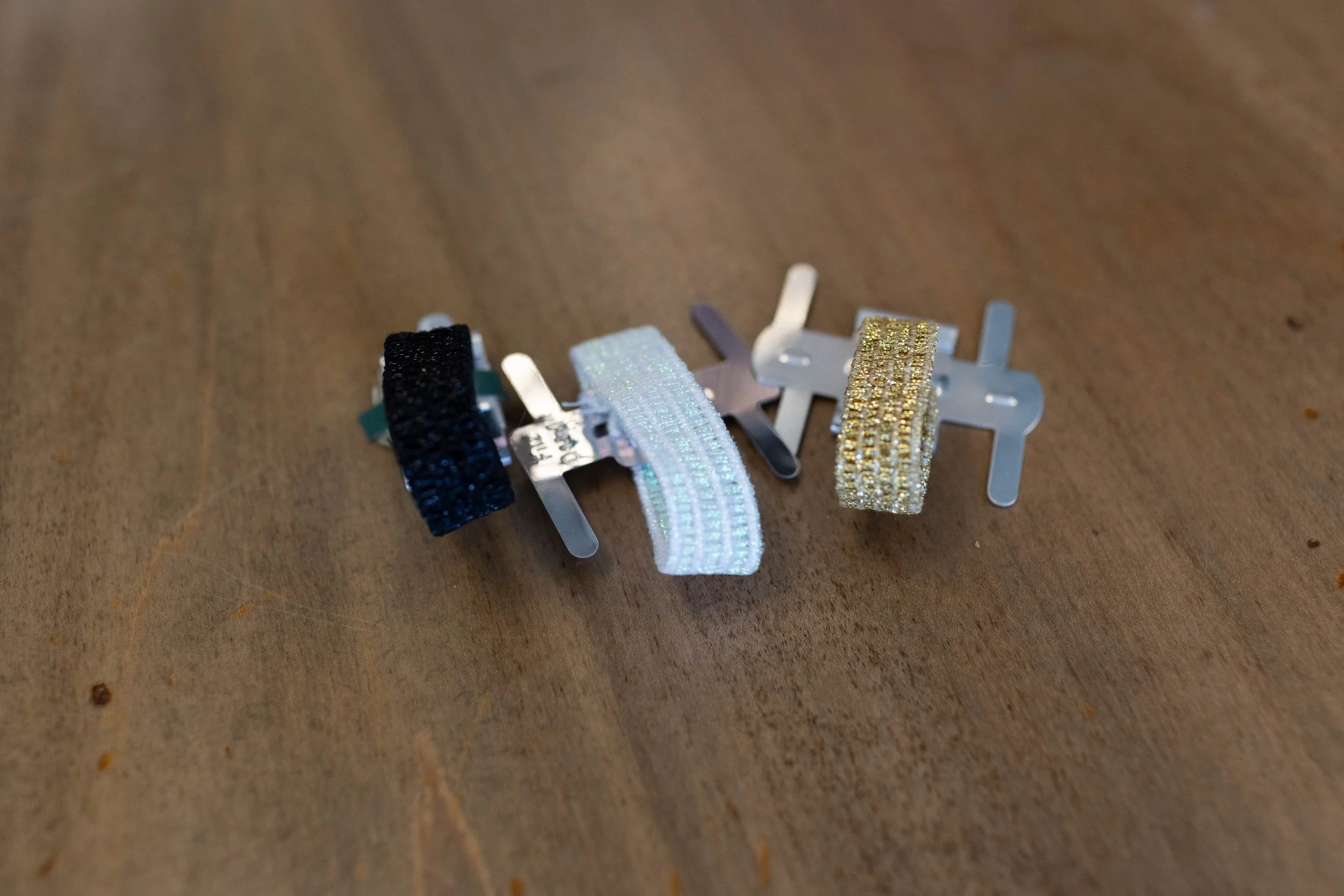Three decorative hairbands with glitter, black, white, and gold, resting on a wooden surface.