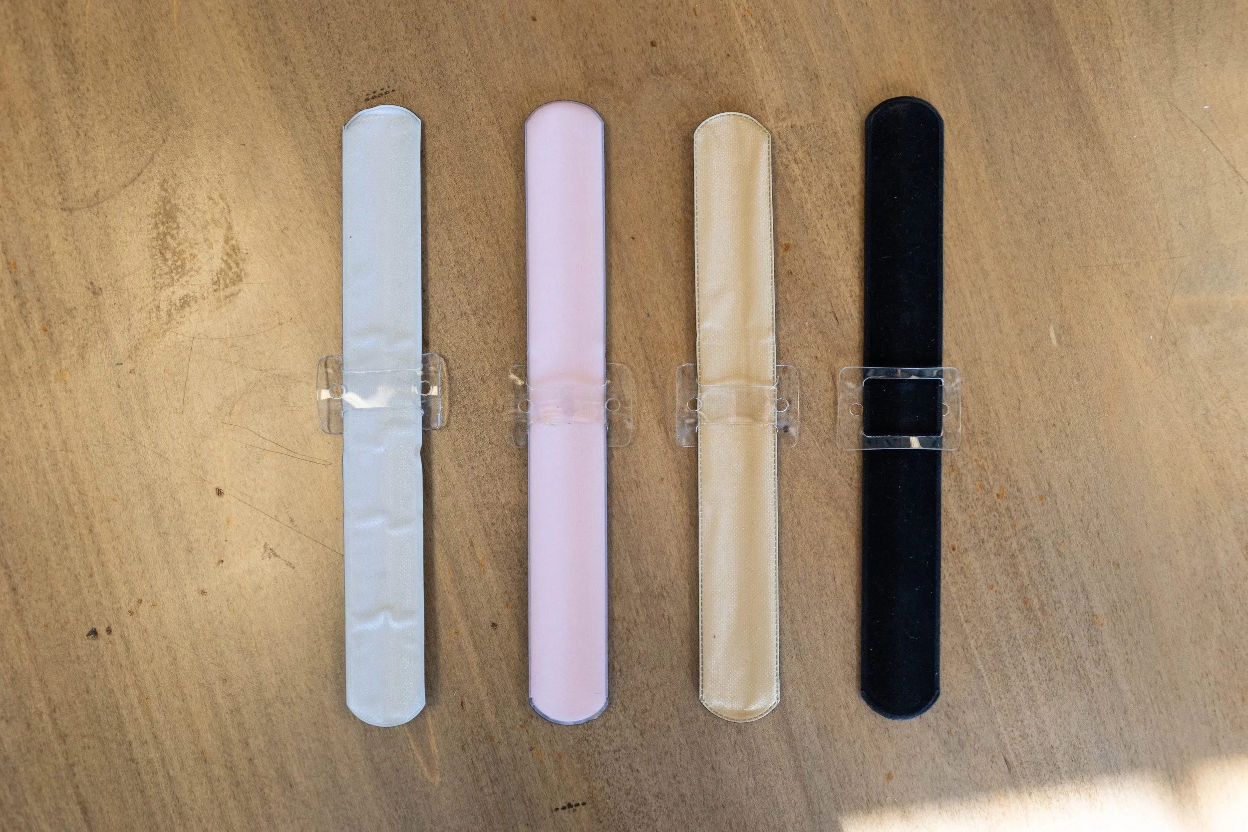 Four fabric headbands in white, pink, beige, and black laid out on a wooden surface.