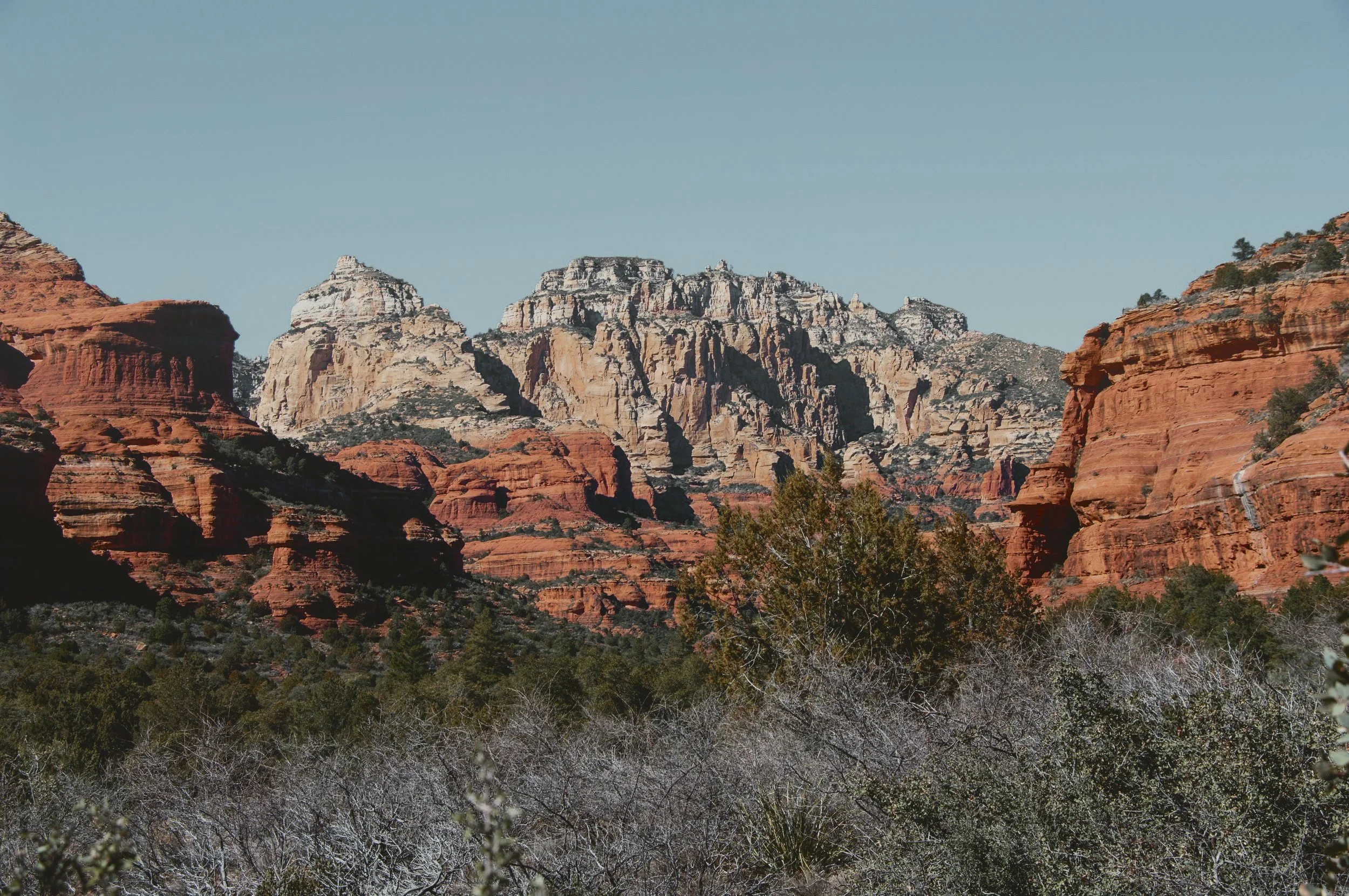 Red and cream sandstone cliffs rising above desert scrub inside Boynton Canyon in West Sedona.