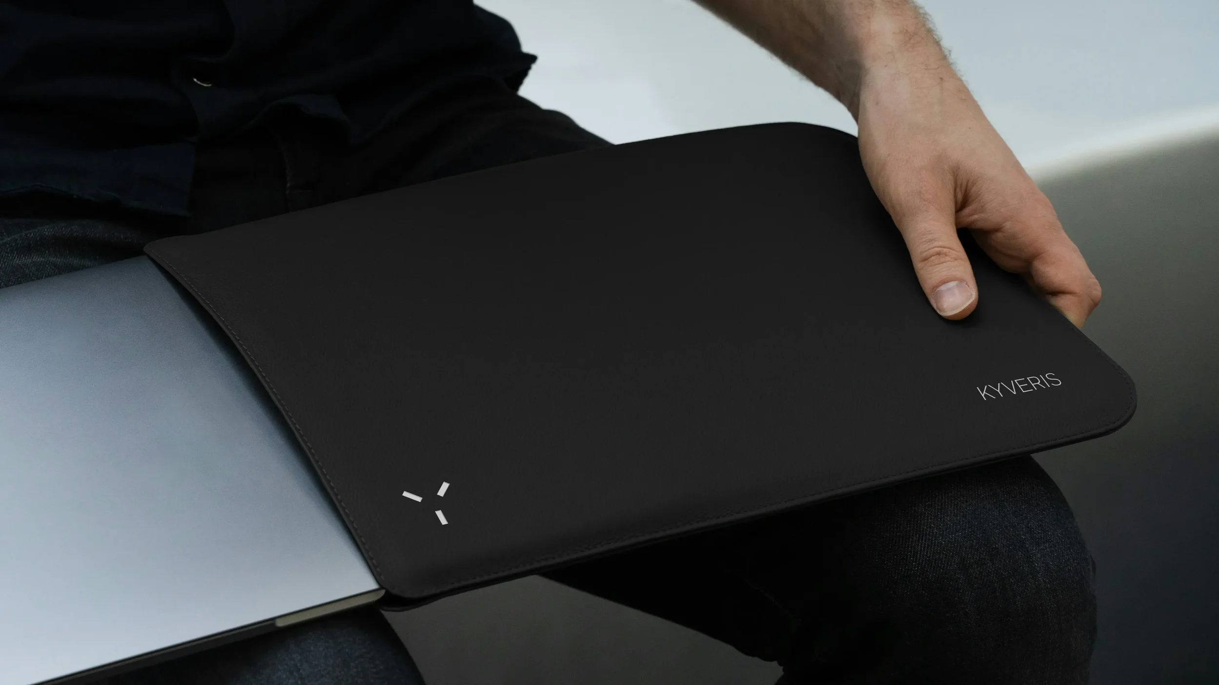 Schwarze Laptop-Hülle mit weißem Logo, von einem Mann gehalten