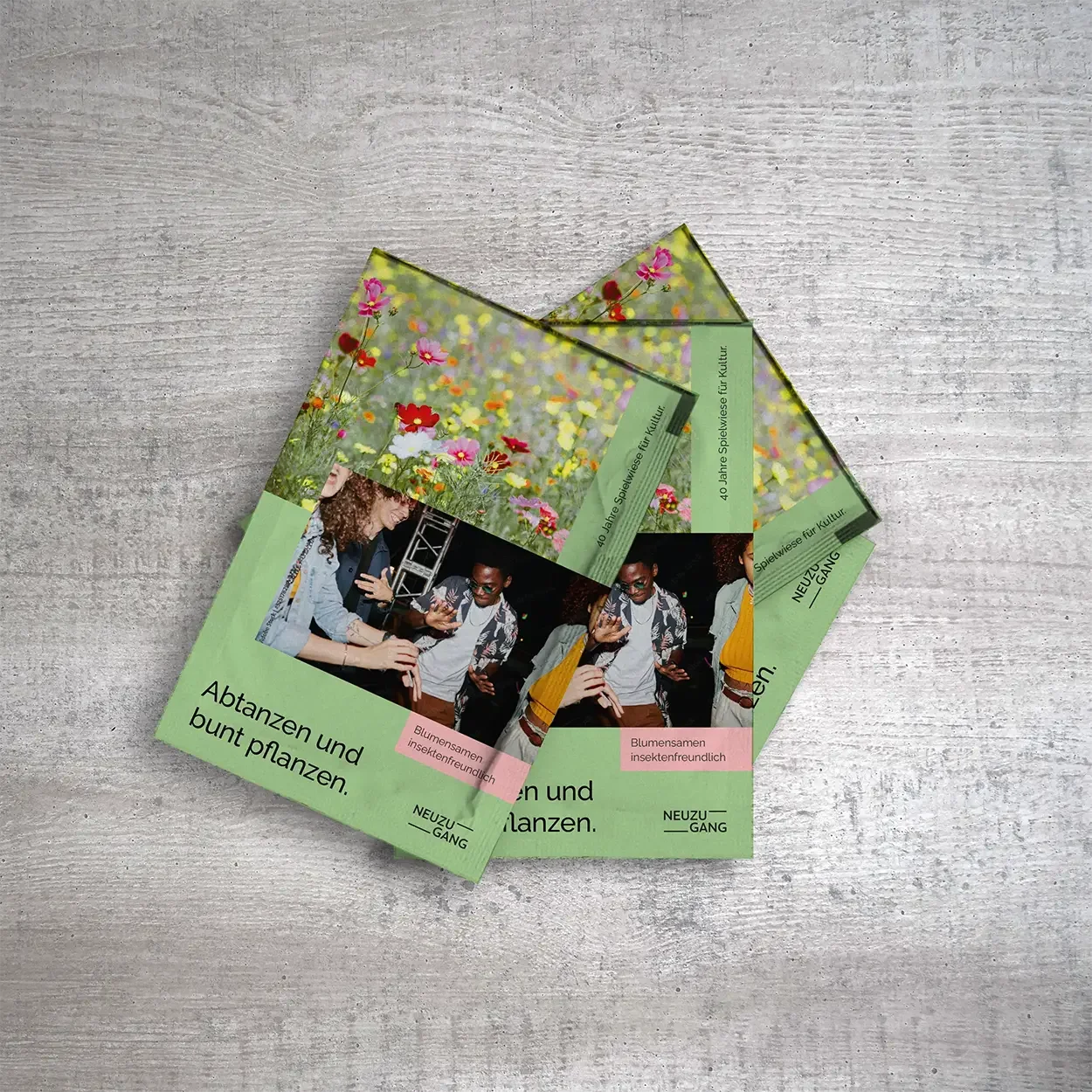 Several colored paper packets, each with a photo of a flower meadow and one of dancing people, lie on top of each other on a gray table.