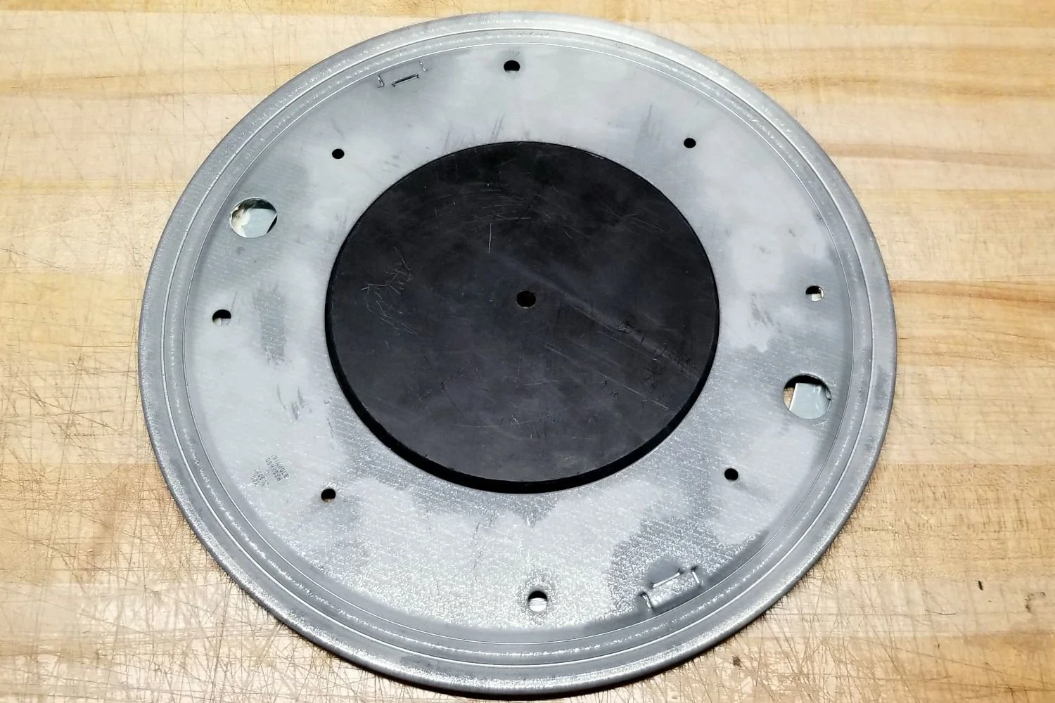 Round metal disc with multiple holes on a wooden surface.