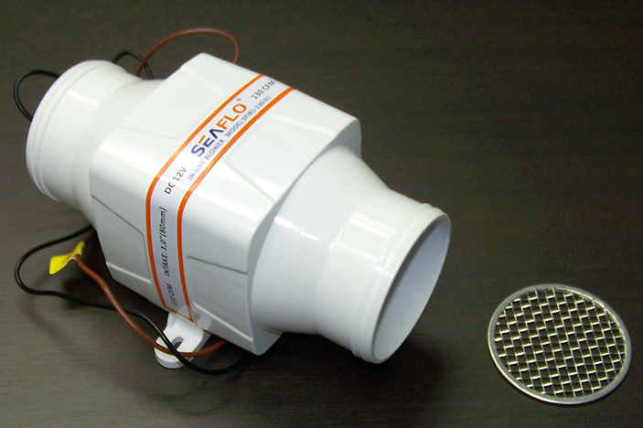 A white, cylindrical submersible water pump with electrical wires, lying on a dark surface, alongside a round metal grille or filter.
