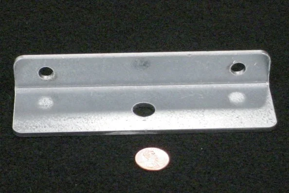A metal mounting bracket with three holes, placed on a black surface with a penny for size reference.