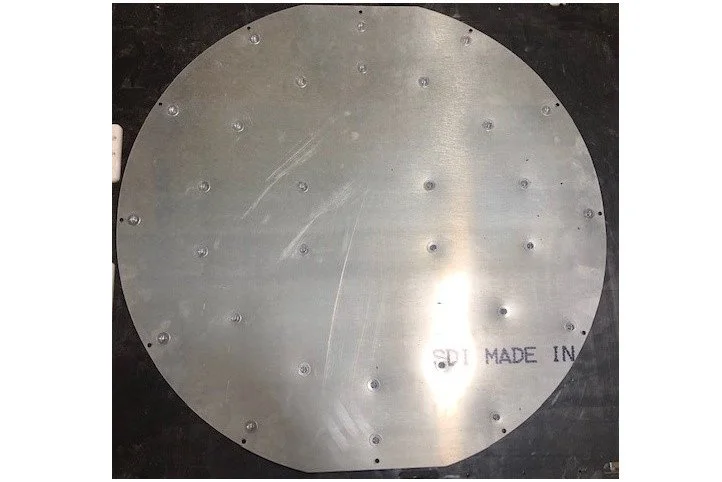 A circular metal plate with multiple small holes arranged around it, and a partial identification mark that reads 'MADE IN' along with some partially visible text.