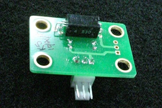 Close-up of a small green circuit board with a black component labeled '830' and a white connector at the bottom, placed on a black surface.