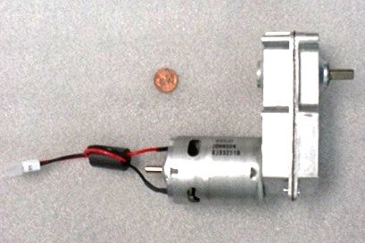 A small DC motor with attached metallic mounting bracket and wires, a copper penny for size comparison, on a gray background.