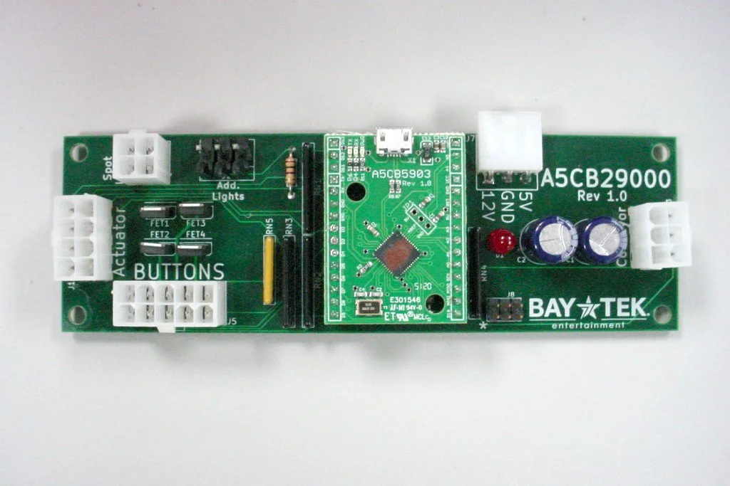 Green circuit board with various electronic components, connectors, and labeled sections, manufactured by Bay Tek Entertainment.