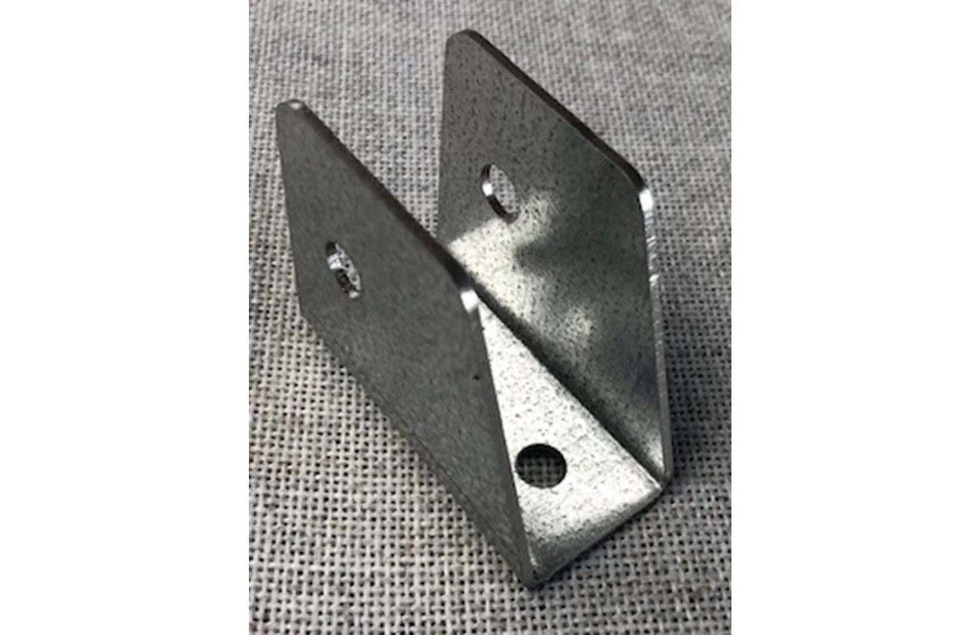 A metal L-shaped bracket with multiple holes, placed on a textured surface.