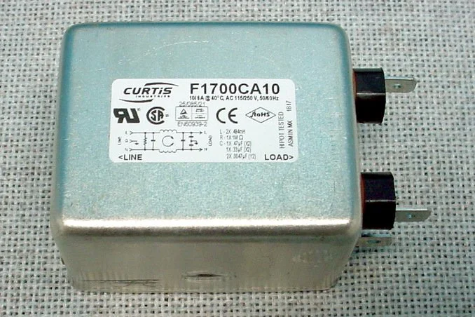 A metallic electrical transformer with a label indicating model number F1700CA10, manufactured by Curtis, with input and output terminals, placed on a textured surface.