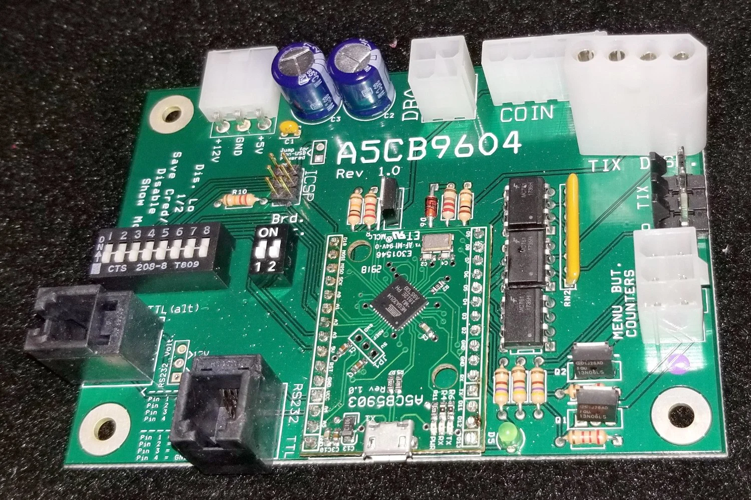 A green printed circuit board with various electronic components, including capacitors, resistors, connectors, and chips. The board has labels such as 'ASCB9604' and 'Rev 1.0'.