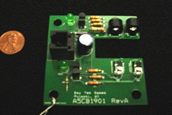 Green circuit board with various electronic components and a small copper coin for scale