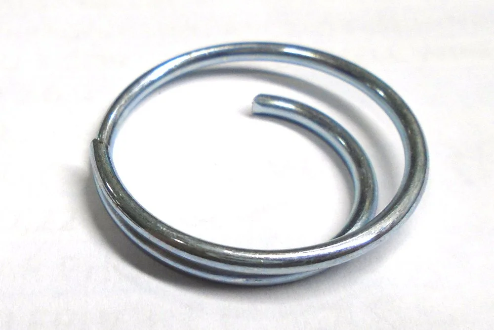 A coiled metal keyring with an open end, placed on a white surface.