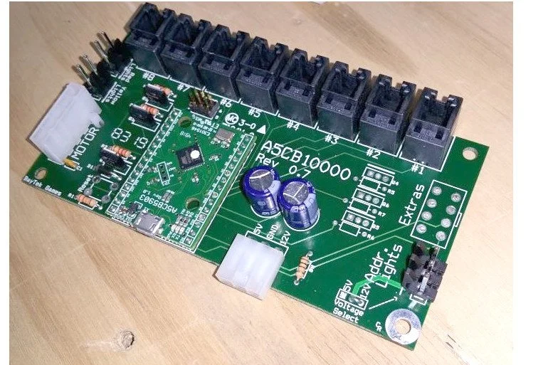 Green printed circuit board with various electronic components including capacitors, connectors, resistors, and switches, labeled as "A5CB10000 Rev 0.7" and "Light Adder Lights".