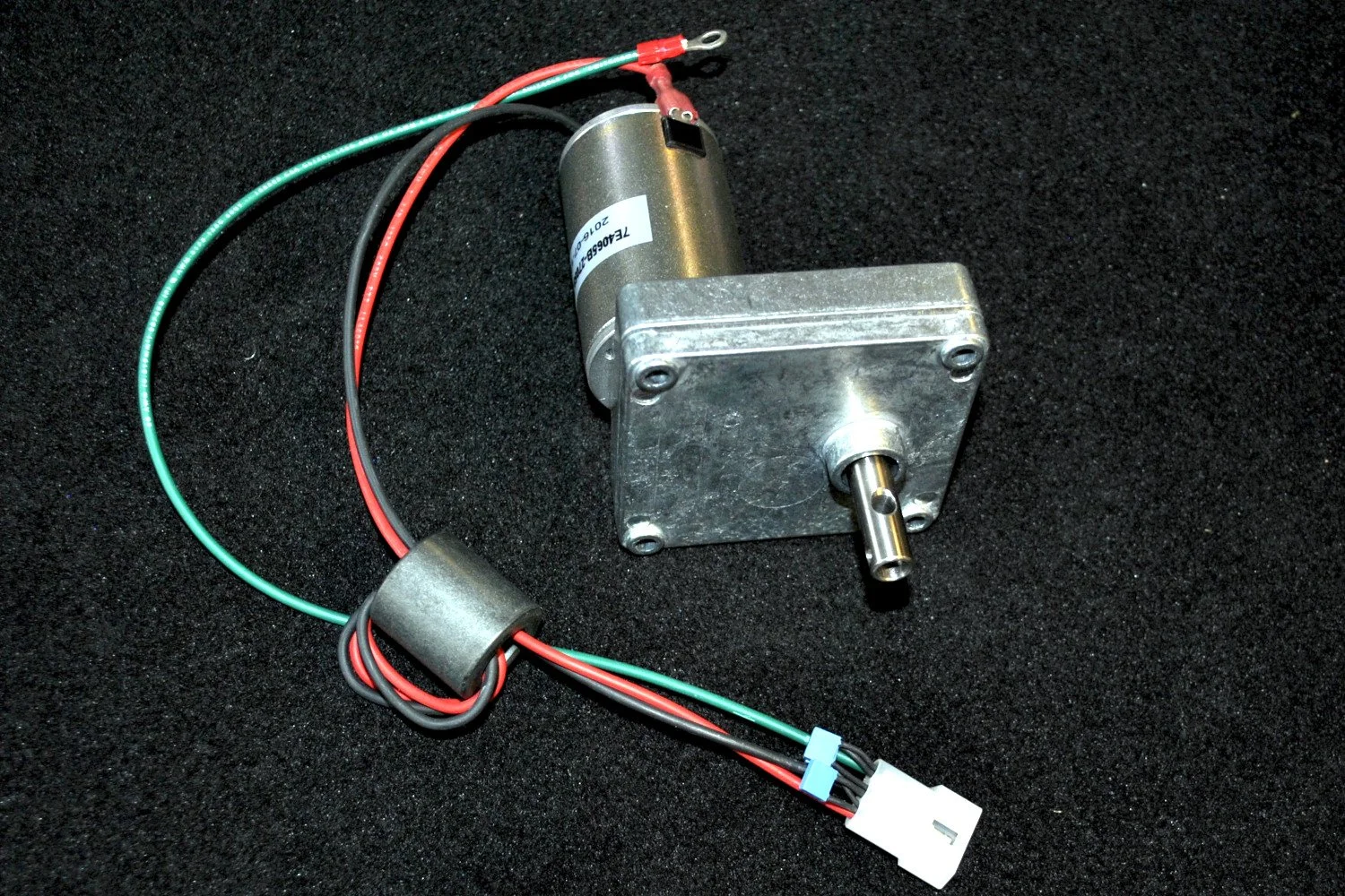 Metal gear motor with attached electrical wires and connector on a black textured surface.