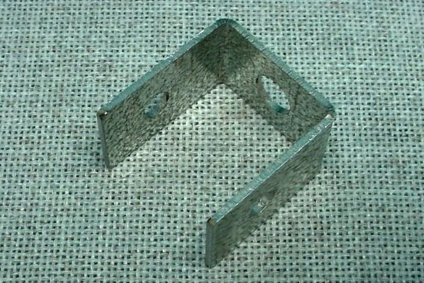 A metal bracket with multiple holes, standing upright on a textured fabric surface.
