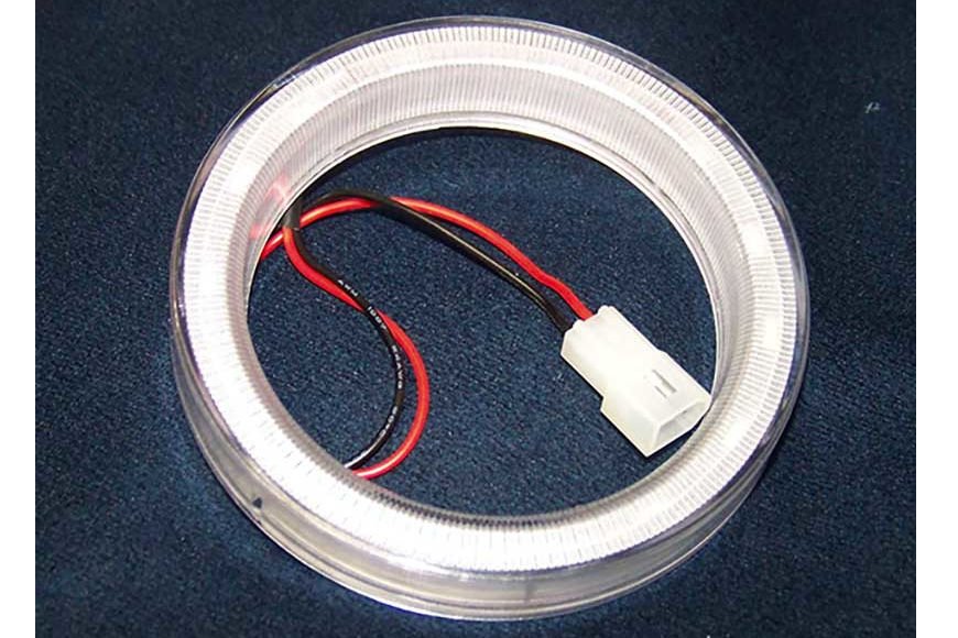 A circular LED light ring with attached wires and a white connector, lying on a dark surface.