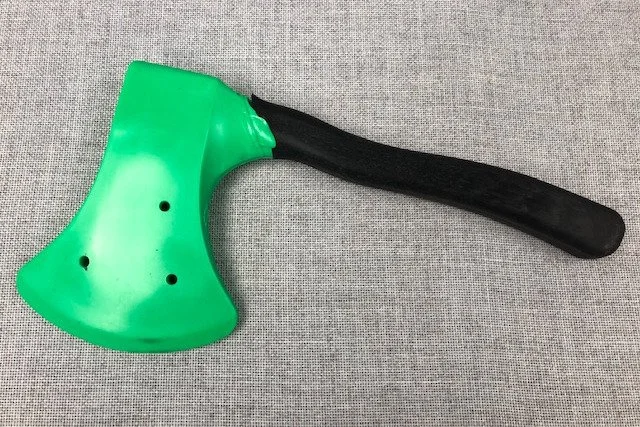 Green plastic axe with a black handle on a gray fabric background.